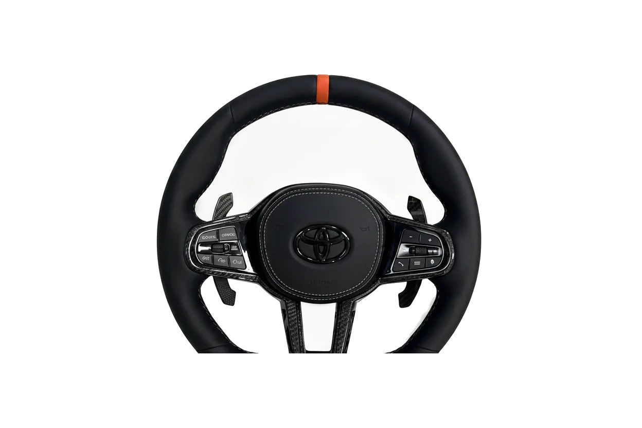 Toyota Supra A90 leather steering wheel with orange centre stripe, carbon fibre trim and paddle shifters on a clean white background